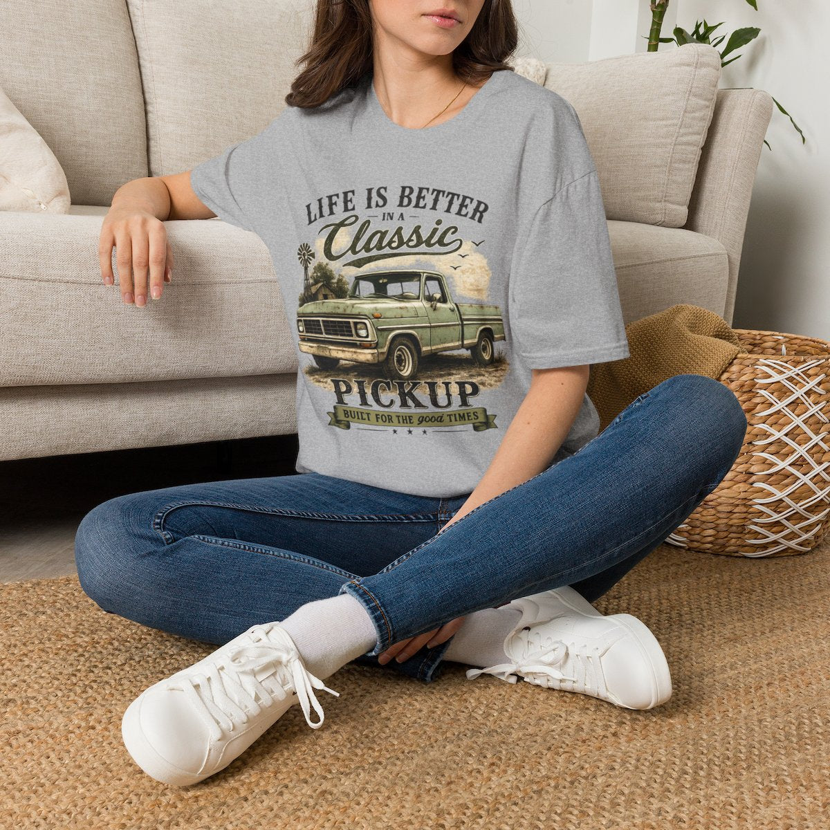 A woman sitting cross-legged on a woven rug in front of a beige sofa, wearing Classic Pickup T-Shirt — "Life Is Better in a Classic" Vintage Truck Tee in Sport Grey