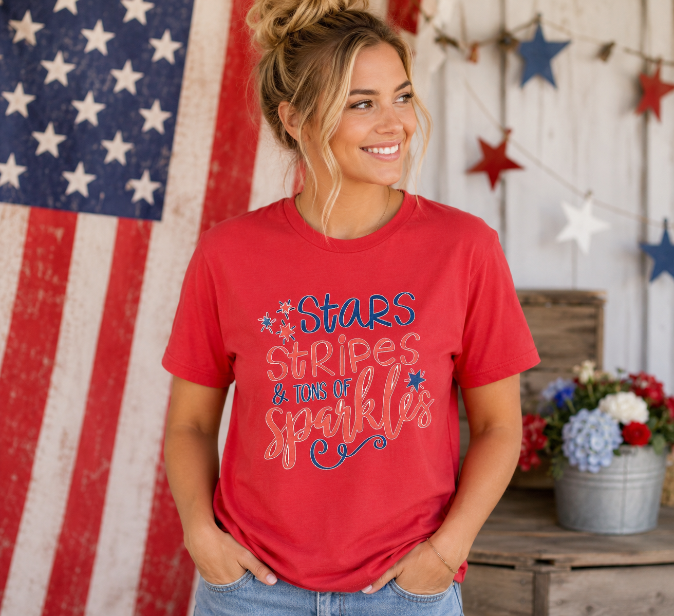 Woman wearing Stars, Stripes & Tons of Sparkles Tee | Women's Medium | Patriotic Graphic Tee in front of an American flag and decorative stars.
