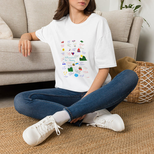 Woman wearing Affirmations for Anxiety Tee | Hand-Drawn Mental Health Graphic T-Shirt sitting on a carpeted floor against a couch with a wicker basket and plant in the background