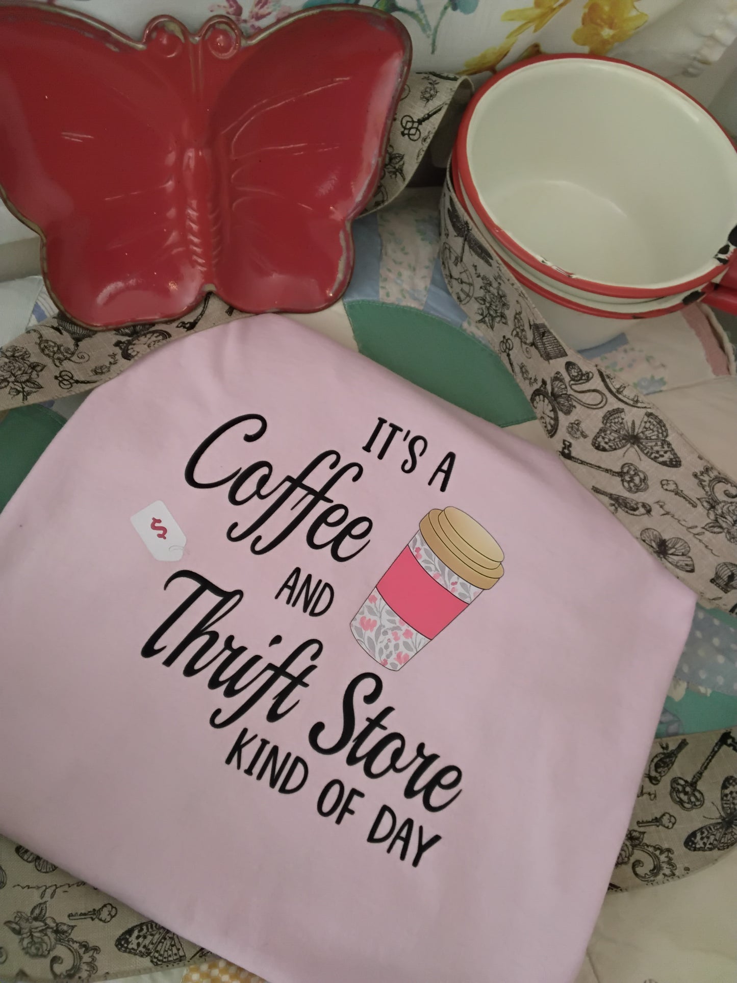 It’s a Coffee and Thrift Store Kind of Day Tee in Light Pink on a background decorated with a butterfly tray, ribbon and old pans